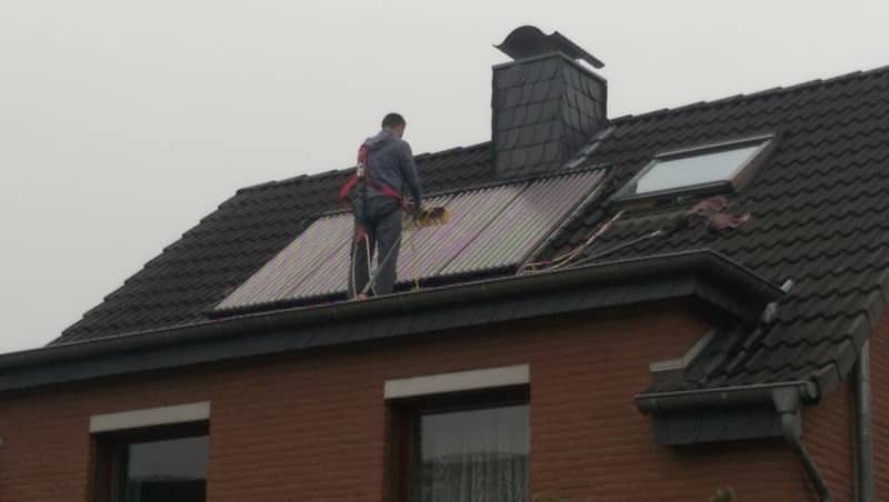 Gesichertes Fachpersonal reinigt Solarpanele auf einem Dach