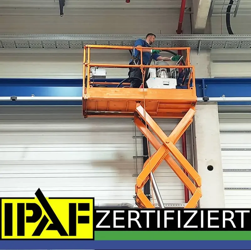 IPAF-zertifizierter PUR-Mitarbeiter auf Scherenarbeitsbühne bei der Höhenreinigung von Industriedecken und Kabeltrassen in Produktionshalle
