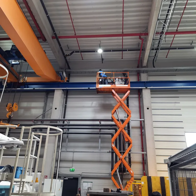 Kranbahnreinigung mit Hubarbeitsbühne — Fachkraft reinigt Laufschiene in Produktionshalle